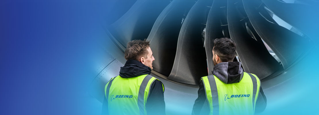 Two people in yellow Boeing vests standing infront of an engine